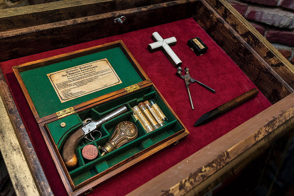 A gun, crucifix, and wooden stake displayed on red velvet