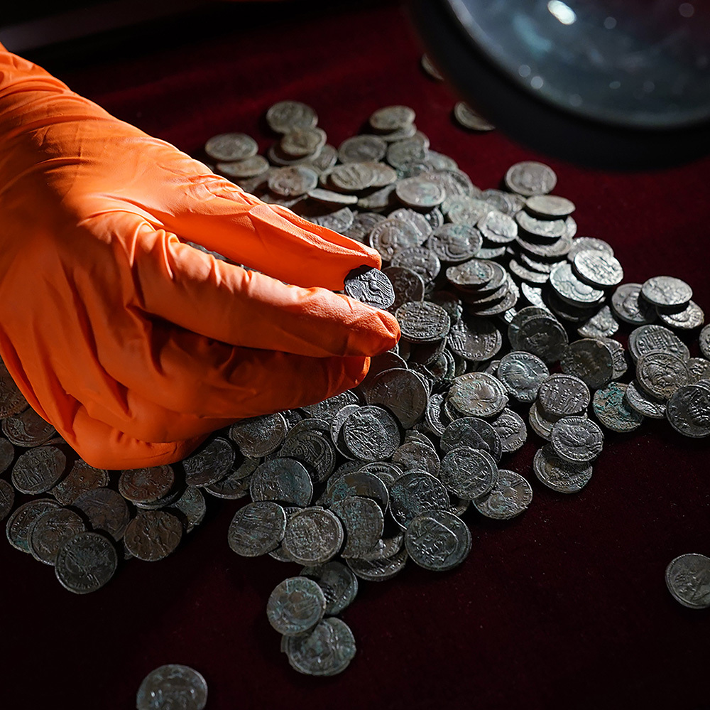 An orange-gloved hand holds a Roman coin on display at the British Museum in London.