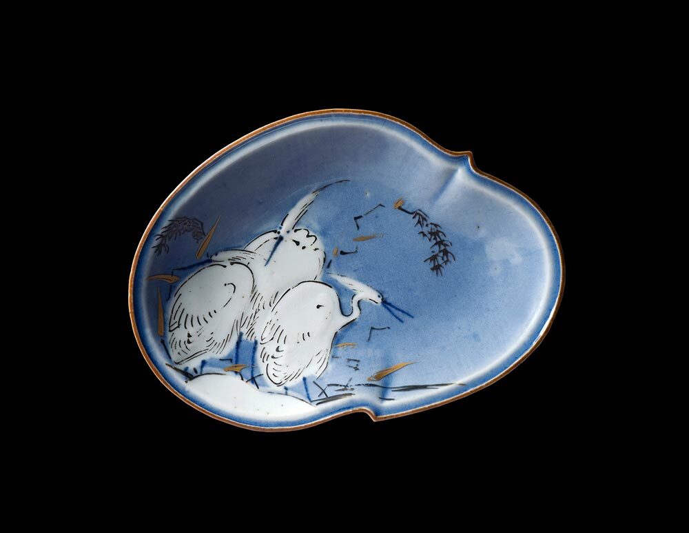 A blue porcelain dish with three white herons against a black background.