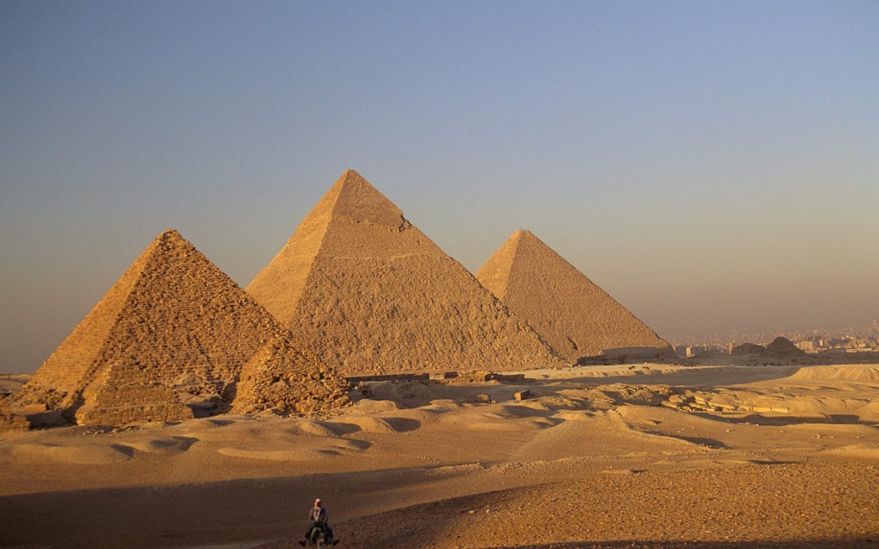 A man rides a donkey through the desert near the Great Pyramids of Giza.