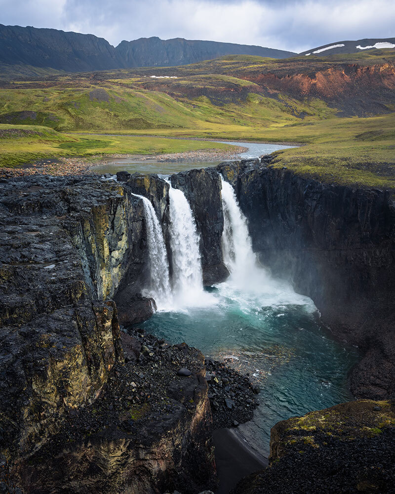 A river among a green plain plunges into a turquoise pool