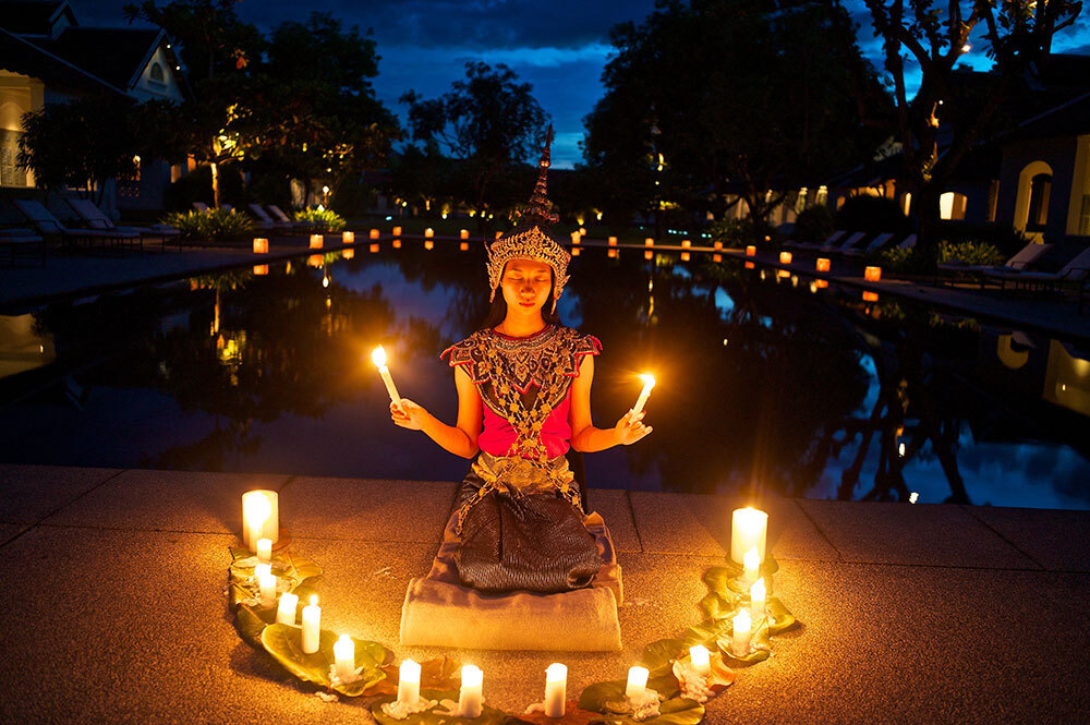 A person in traditional clothing sits in a semi-circle of candles