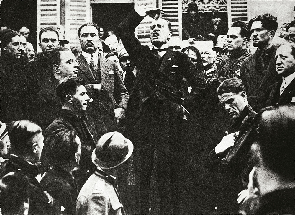 A black and white picture of a man giving a speech in a crowd