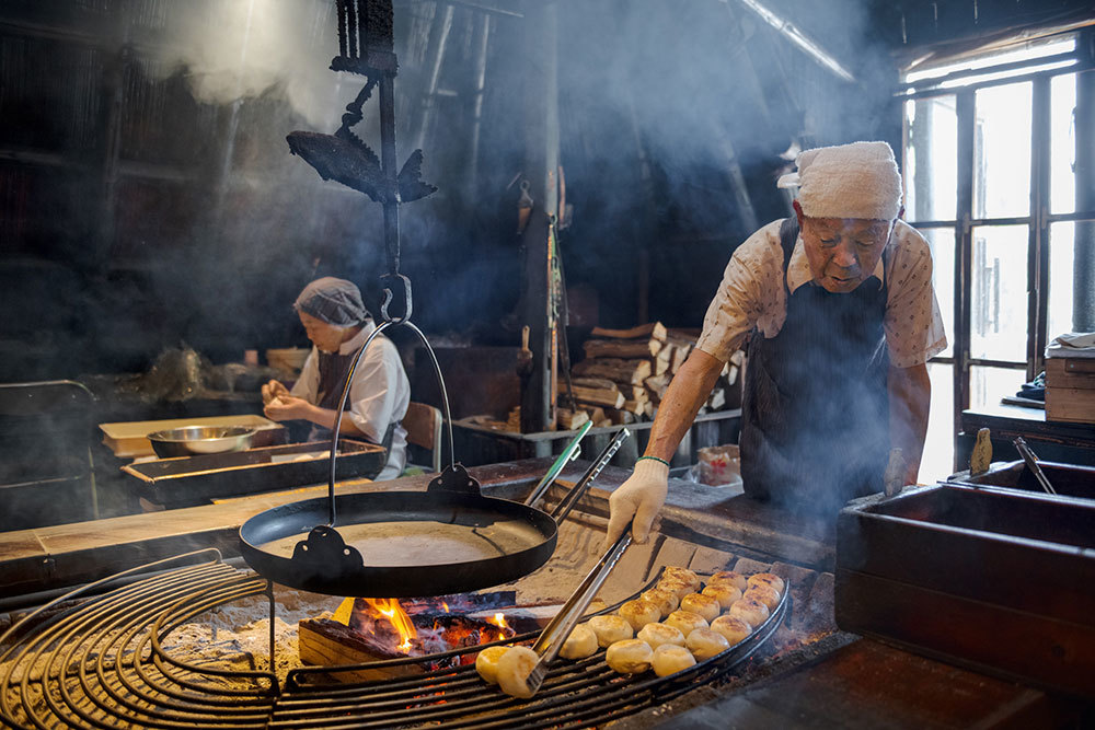 An elderly person cooks over an open flame