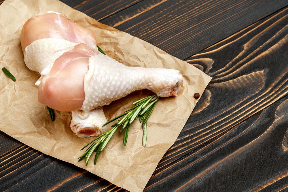 raw chicken on a table with a sprig of rosemary