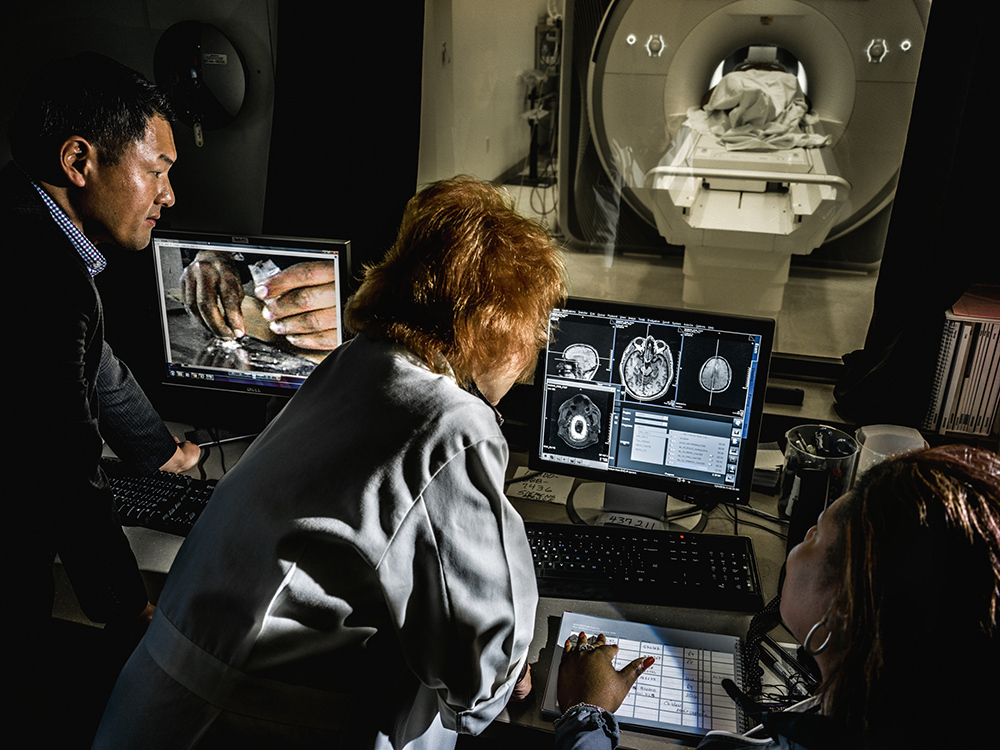 Scientists and doctors looking at brain scans while person in background is in MRI