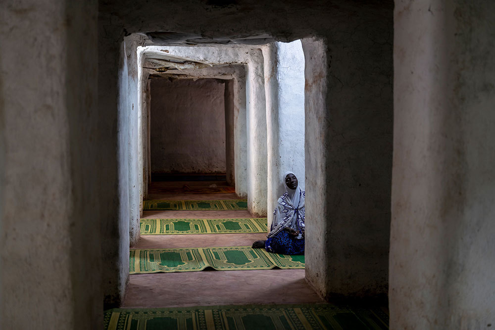 A picture of a woman sitting in a hallway made of smooth earthen walls