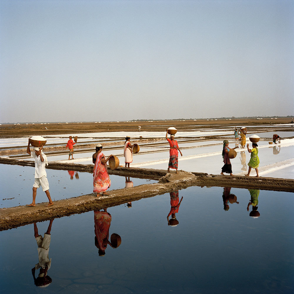 A picture of a people carrying baskets of salt between pools of water