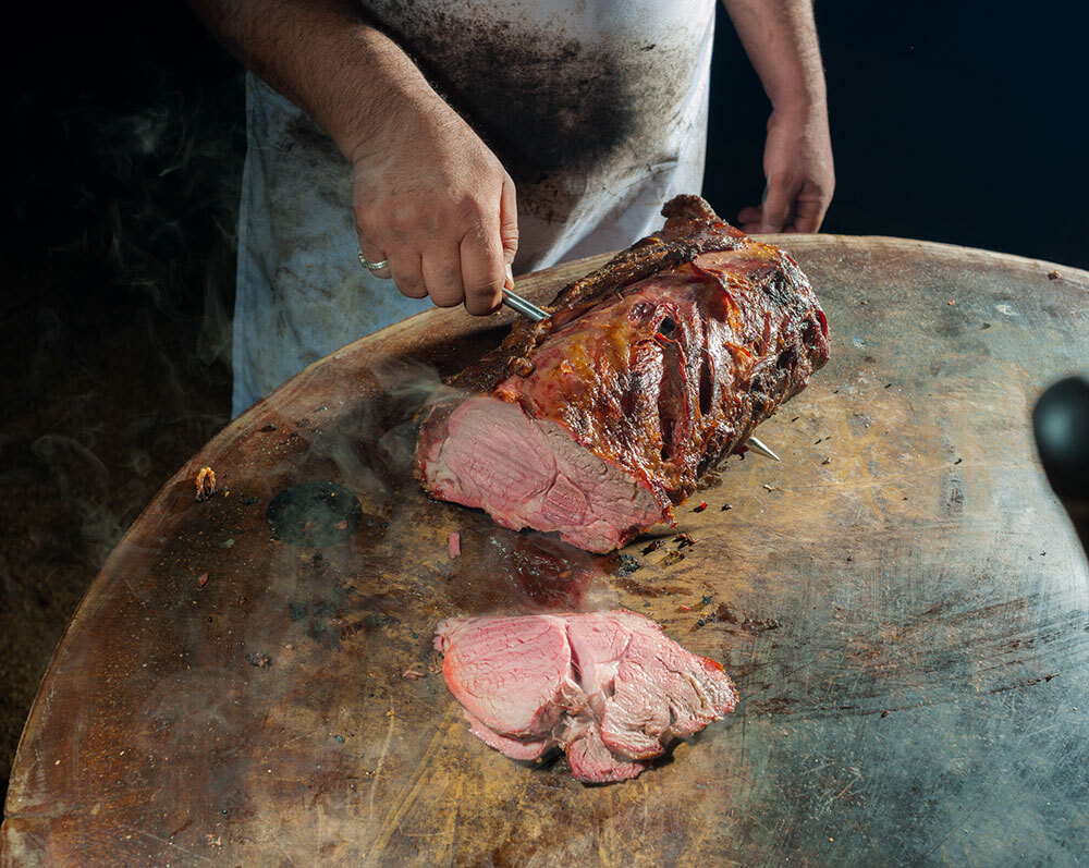 a man cuts a slab of meat sitting on a table