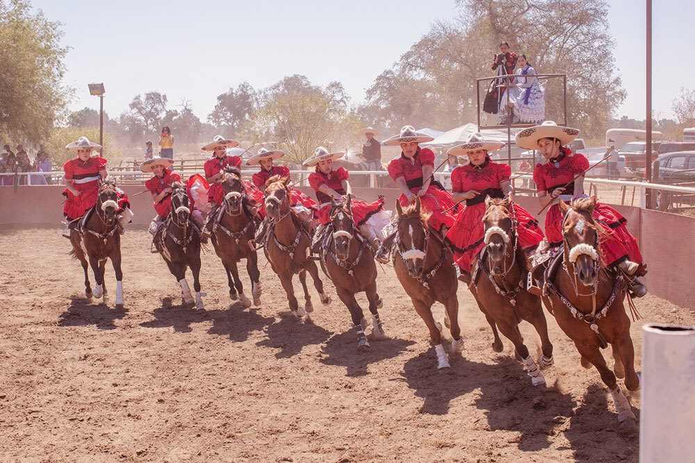 In Snelling, California, female equestrians known as escaramuzas wearing dresses and embroidered sombreros perform a synchronized horseback ballet at a full gallop as part of charreadas—Mexican rodeos.