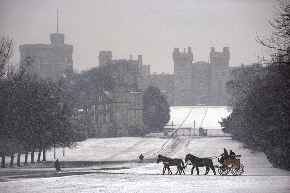 Prince Philip drives a horse-drawn coach in front of a snow-covered Windsor Castle