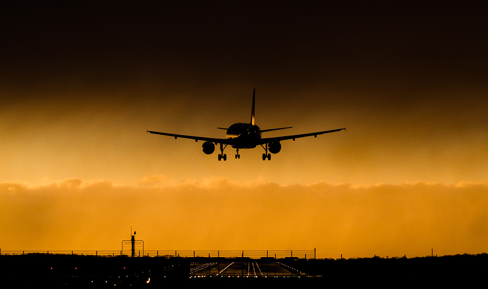 An airplane landing beneath a curtain of dark clouds; the plane is crooked in its approach due to the high winds