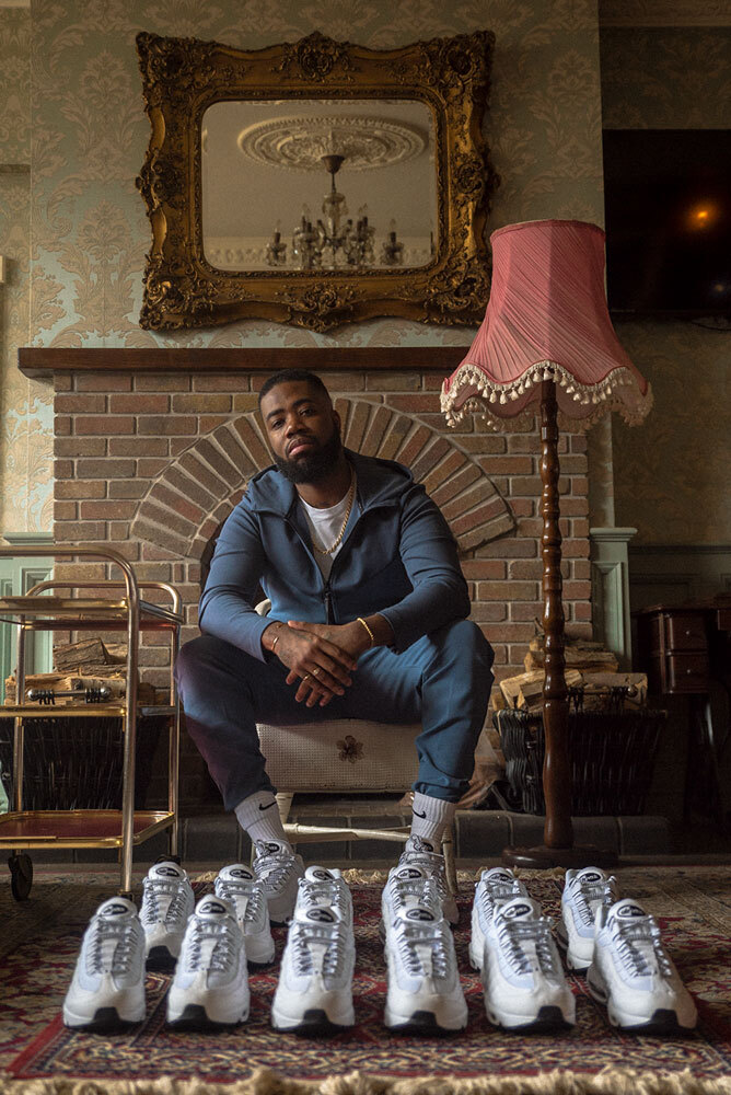 a man sits in his living room with a dozen white sneakers displayed in front of him