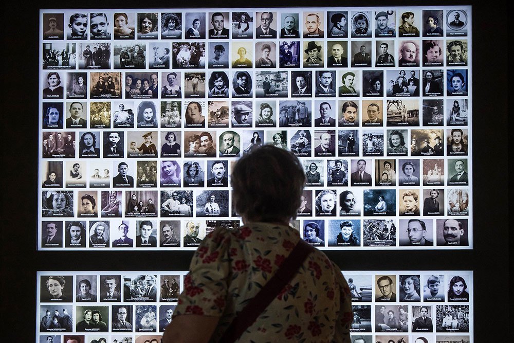 A picture of a woman looking at a wall covered in portraits