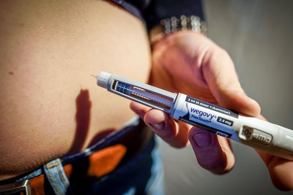 A close-up view of someone holding a Wegovy multi-dose injection pen beside their exposed belly.