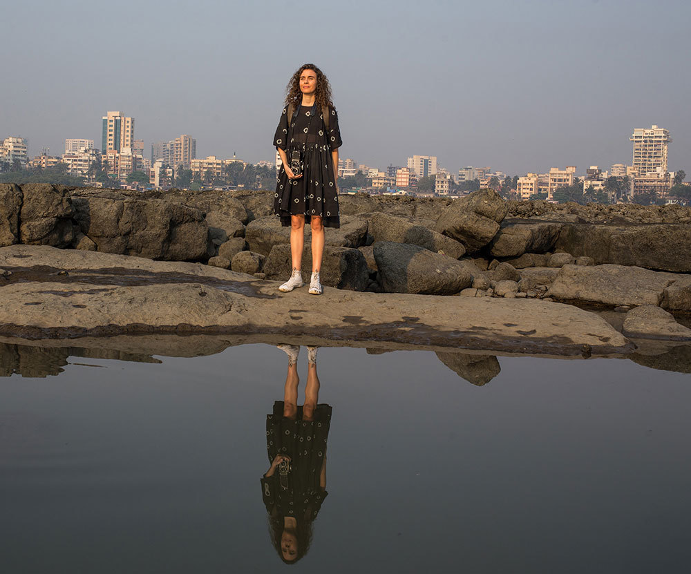 A picture of a woman holding a camera with the Mumbai skyline behind her