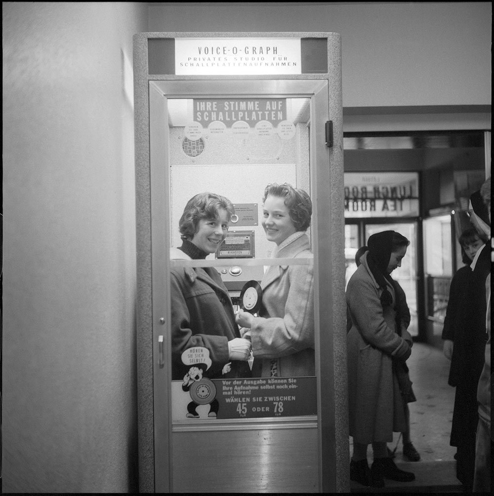 A black and white picture of two women in a booth holding a record