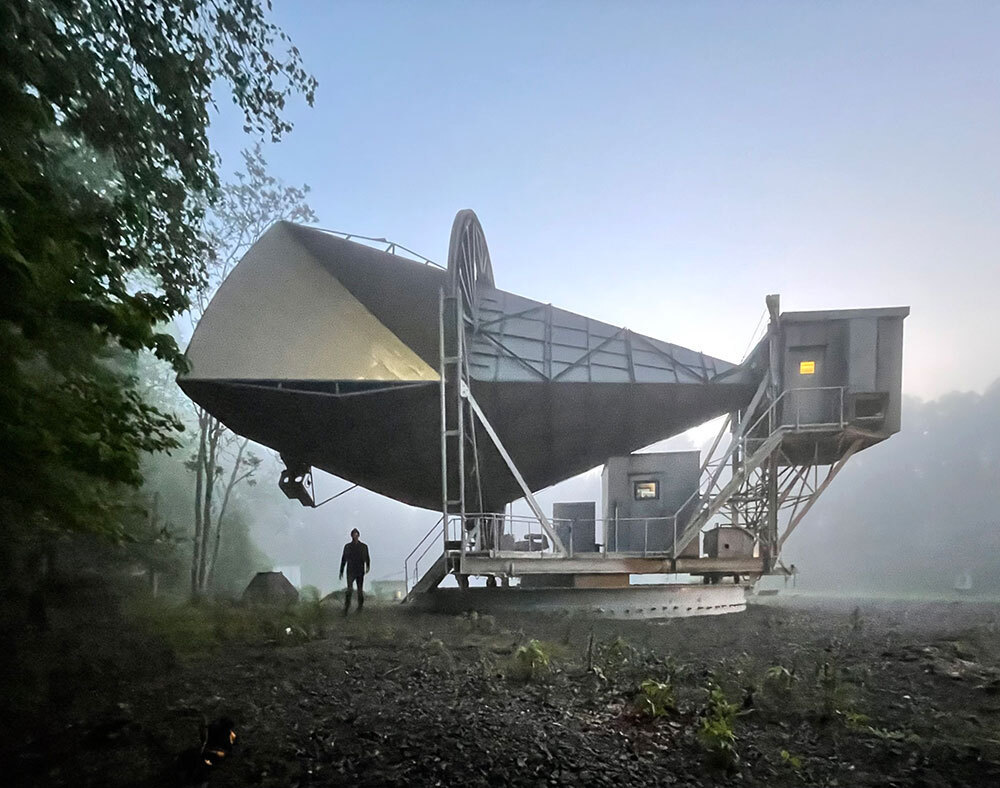 A man stands below a giant metal cone in the fog