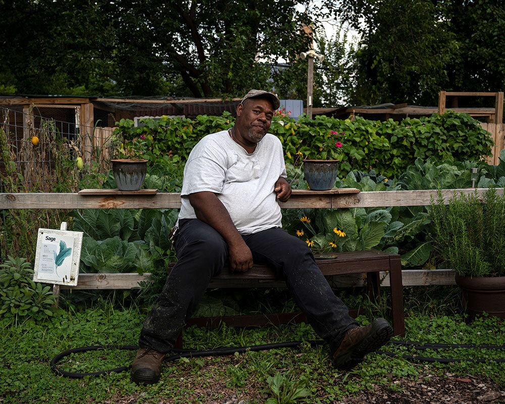A man sits on a bench surrounded by plants