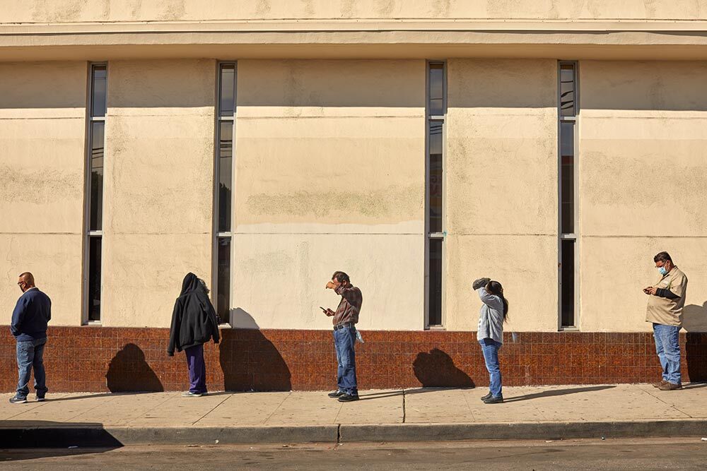 People standing in line as the midday sun shines brightly down.