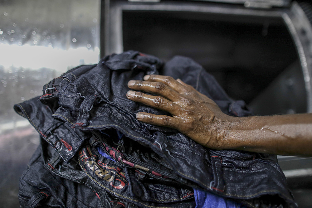 The hand of a worker unloading jeans from a fabric dyeing machine at a factory