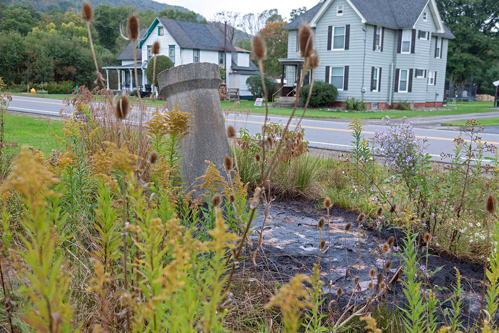 A concrete pipe surrounded by dark sludge pokes out of the ground in front of residential houses