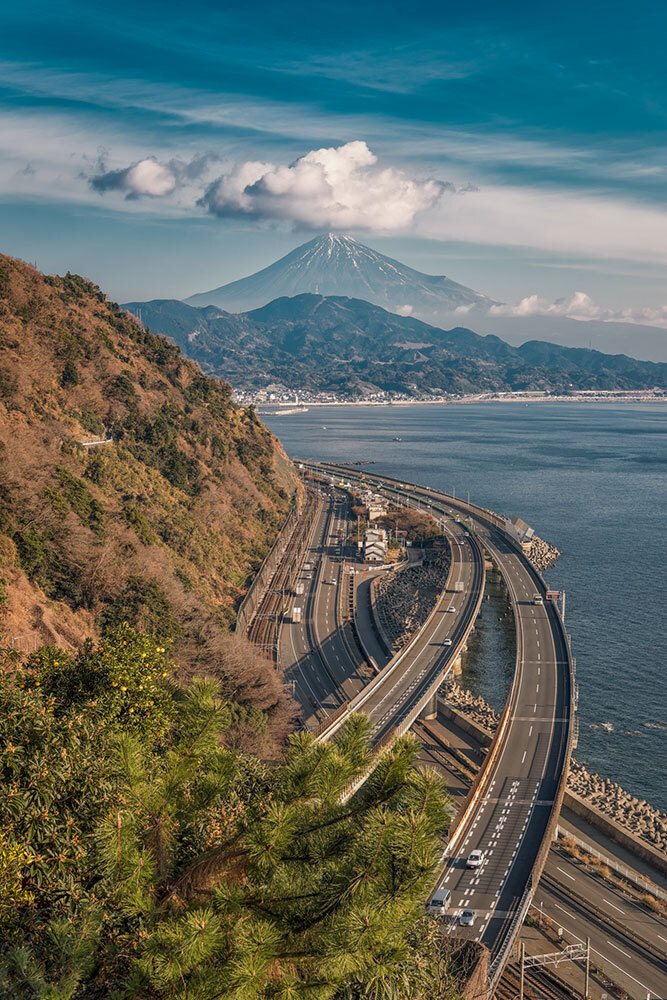 Cars wind around a mountain on a highway towards Mount Fuji