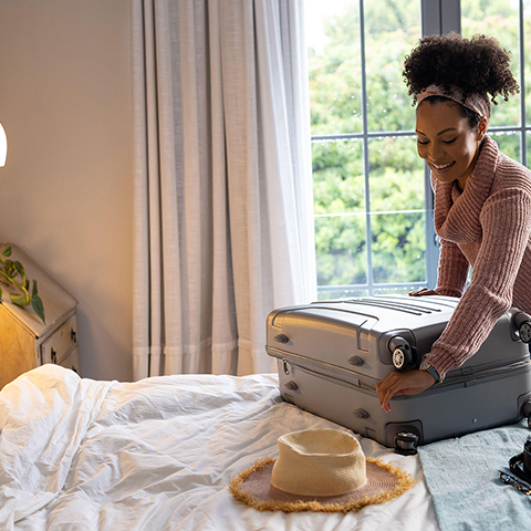 A black men bent over a suitcase as he gently packs his clothes.