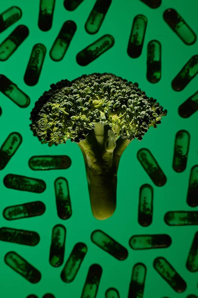 A conceptual photograph showing a floret of broccoli on a green background of multivitamin capsules