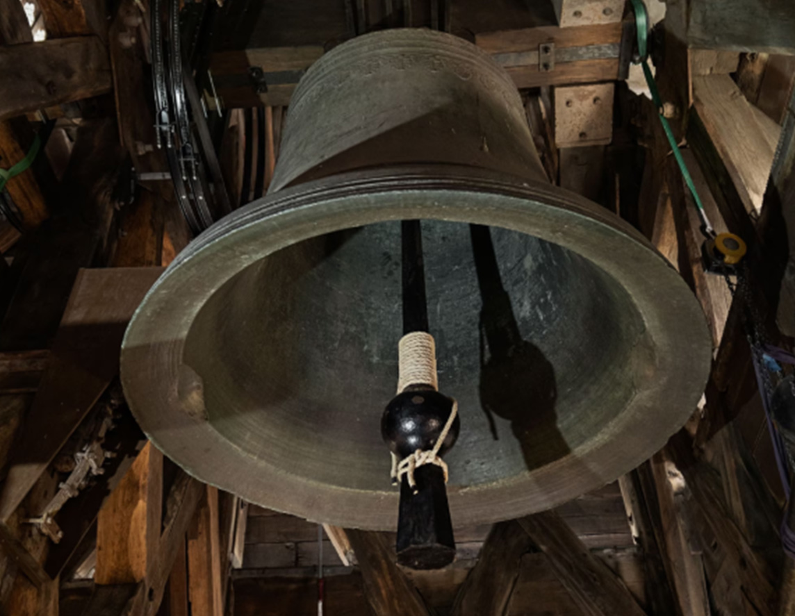 A large bell photographed from below is seen suspended from the tower