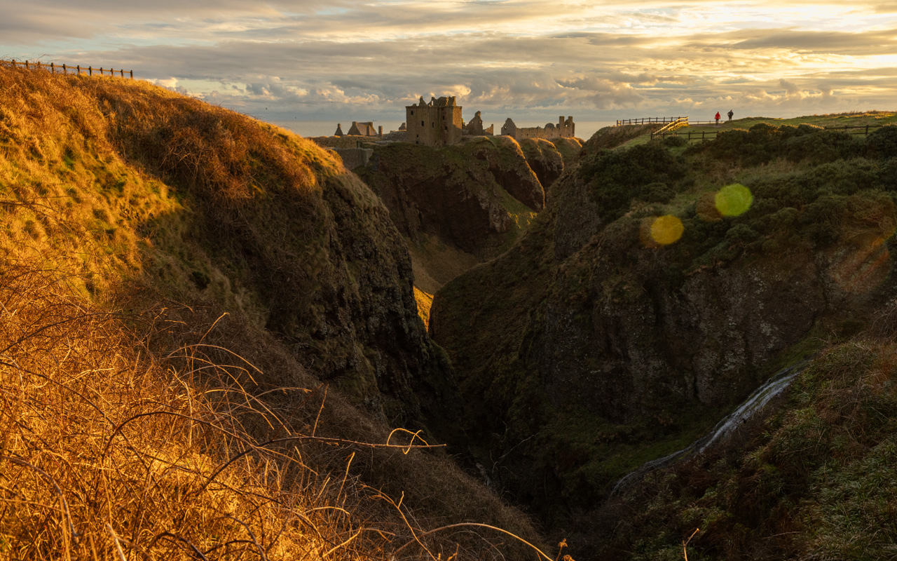 Dunnottar Castle standing tall in the distant backdrop, surrounded by scenic beauty.