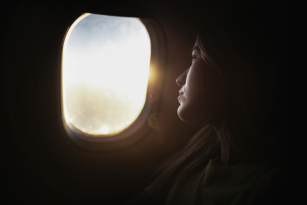 A woman's face, lit by soft, warm light as she looks out an airplane window