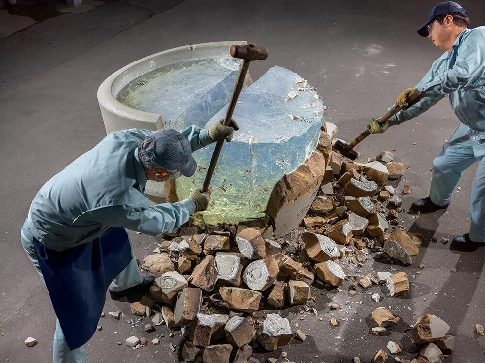 Workers at the Chiba Kogaku glass factory use sledgehammers to remove the clay pot around a core of optical glass.