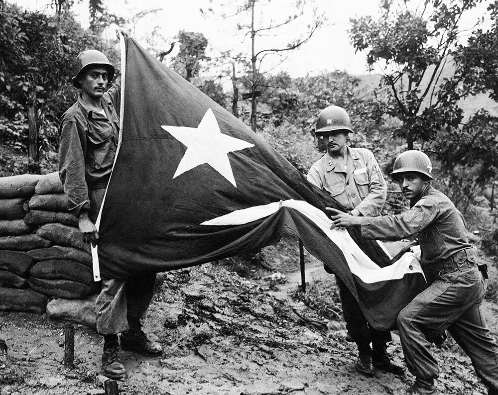 Members of the U.S. Army's 65th Infantry Regiment, also known as "The Borinqueneers," hold a Puerto Rican flag, using a finger to show one of the holes in the flag riddled with shellfire during the war in Korea in 1952.