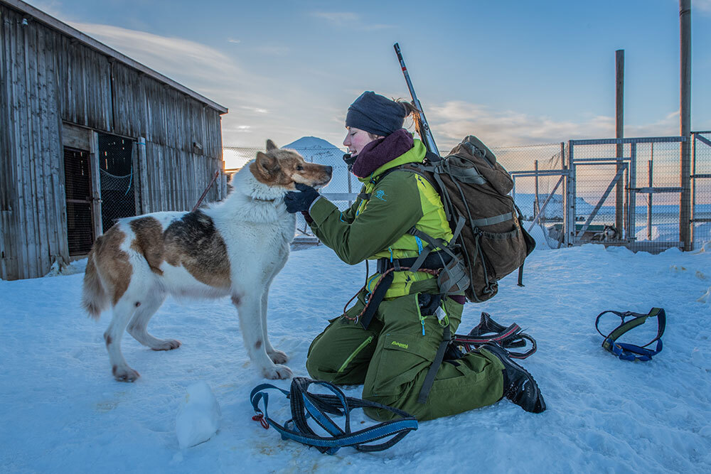 A picture of a person in snow gear petting a dog