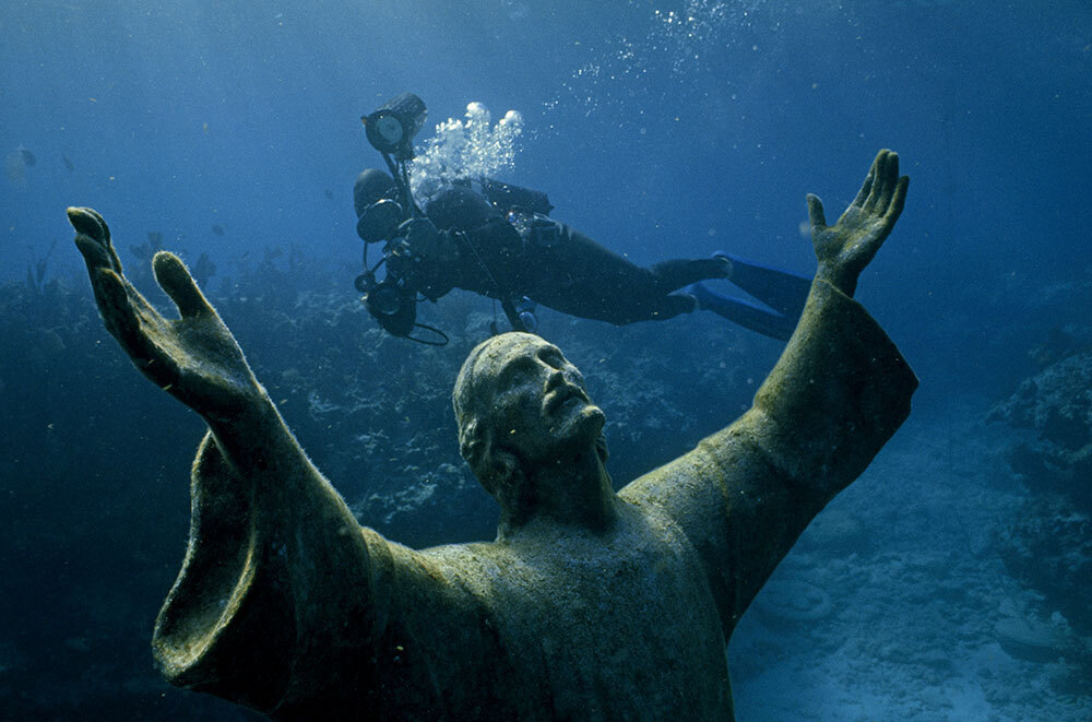 A picture of a scuba diver taking a photo of a submerged statue.