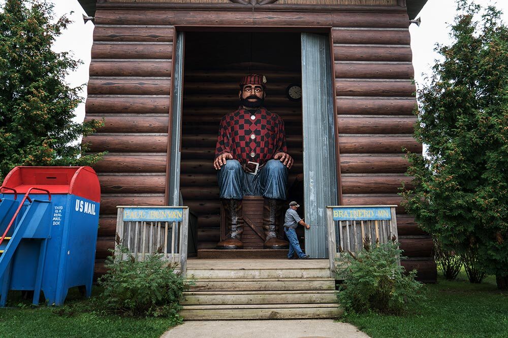 A man closes a shed door containing a larger-than-life Paul Bunyan.