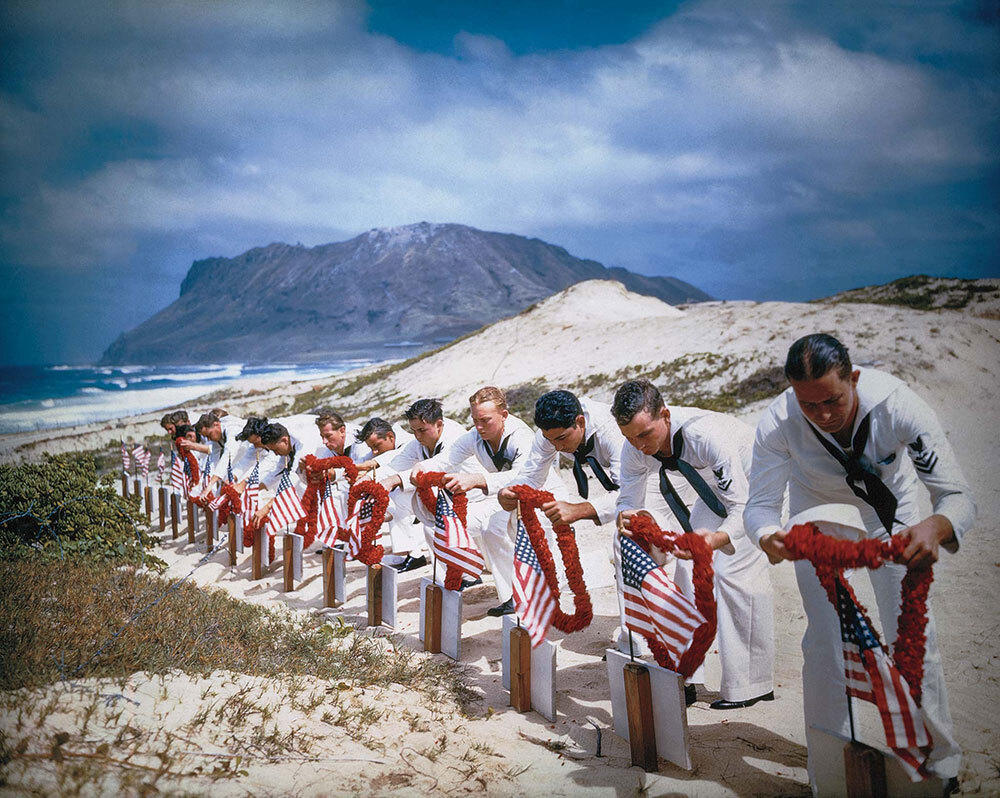 A picture of men laying flower necklaces on tombstones