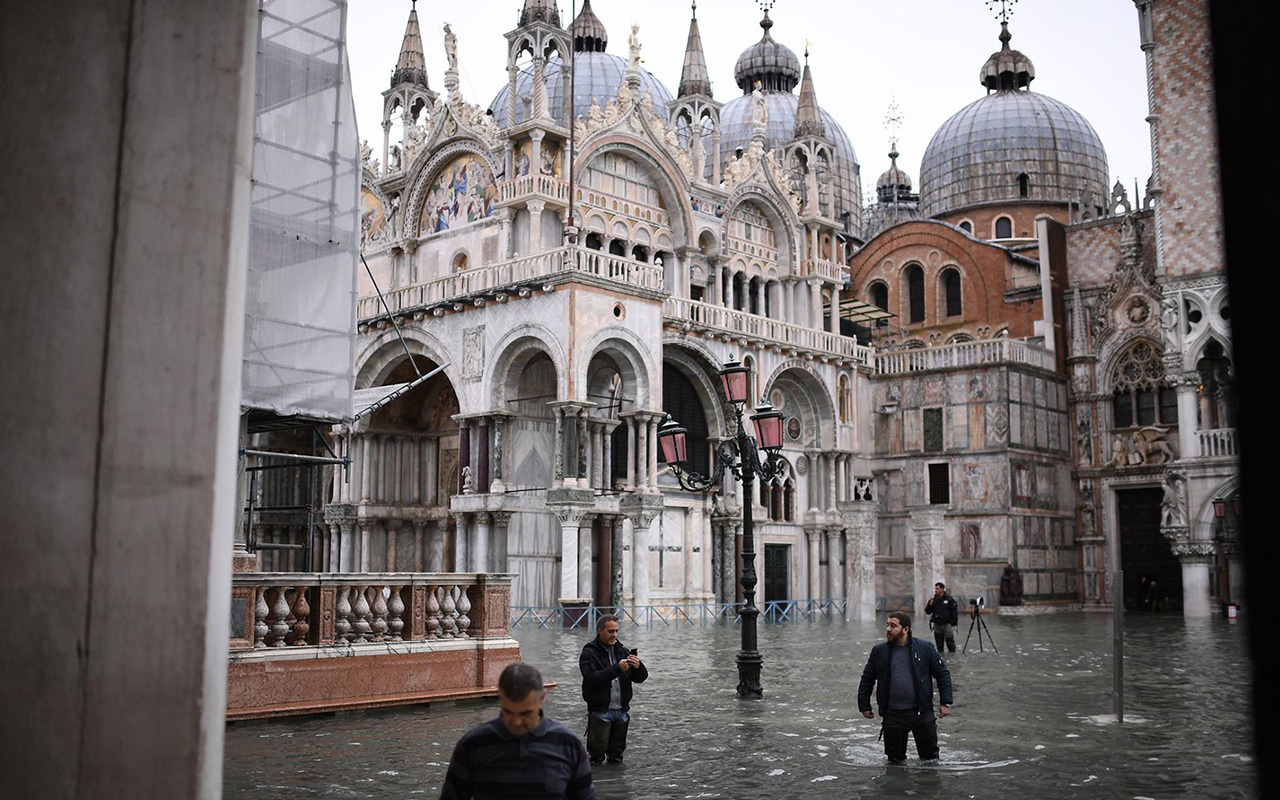 Wearing thigh-high rain boots, pedestrians cross flooded St. Mark's Square in Venice. An exceptional high tide, seasonal winds, and storms have driven flood levels to a 50-year high.