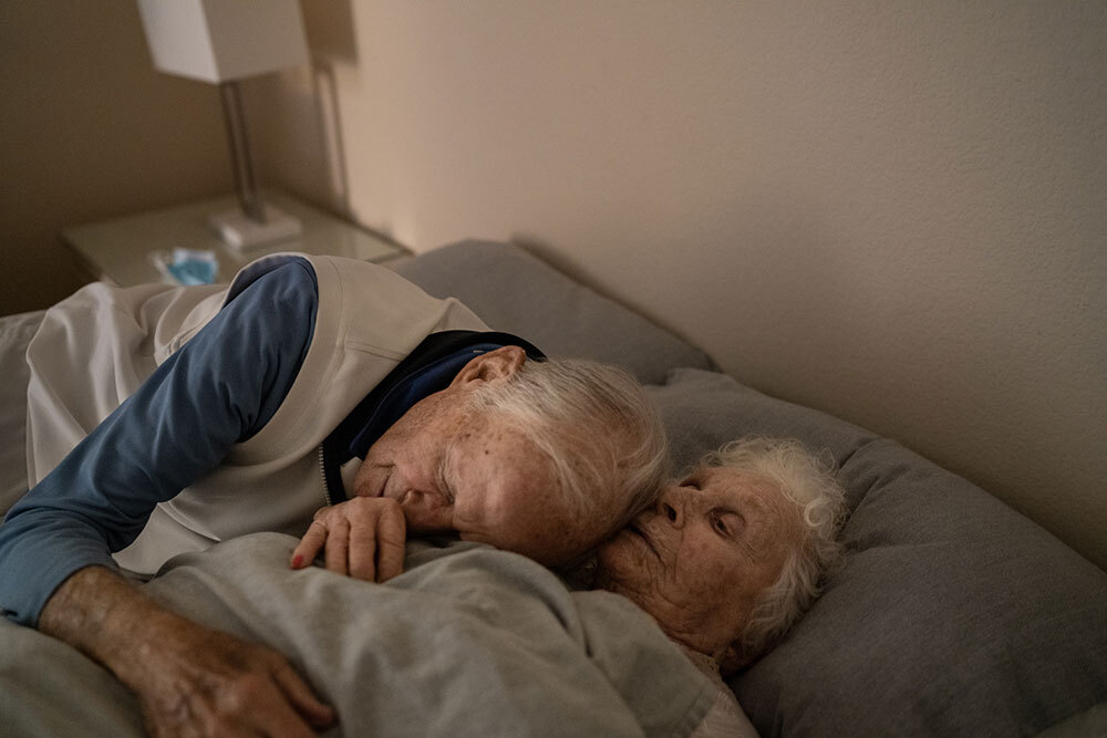 Elderly man embracing his wife at night on their bed in the memory care area.