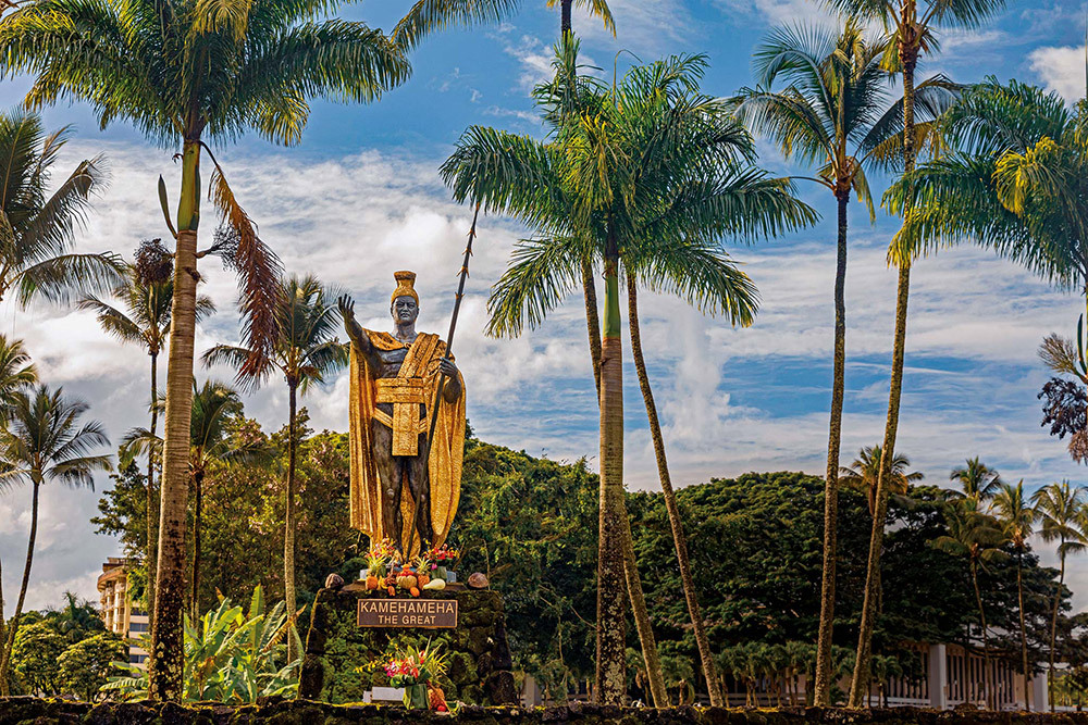 A 14-foot-tall statue of King Kamehameha stands in a park with palm trees