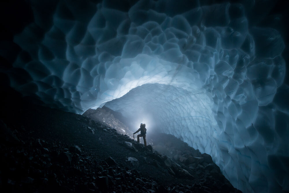 An expedition member is seen silhouetted as they stand in a tunnel of smooth, wavy-textured ice.