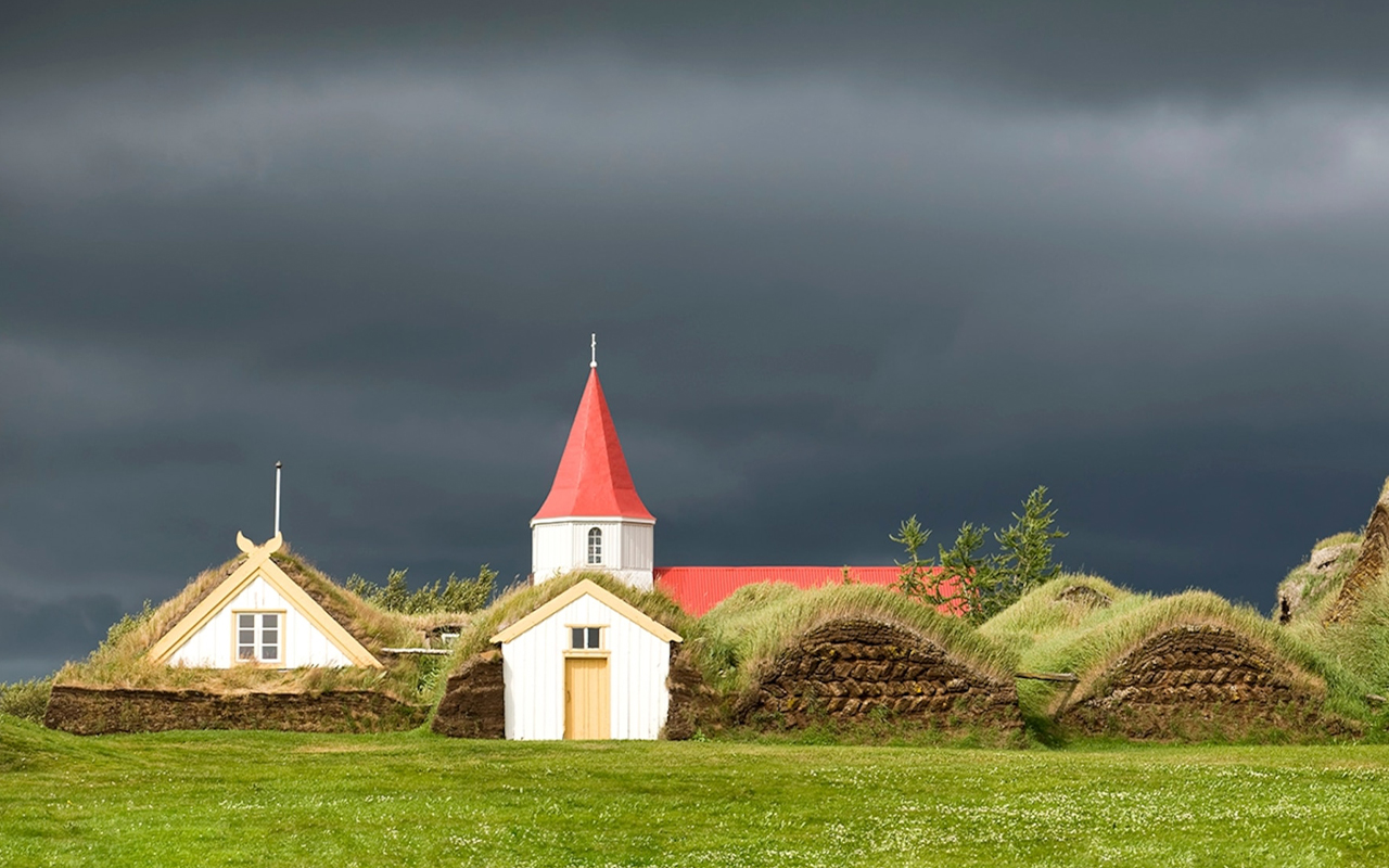 Dark clouds roll over a turf house and church in Glaumbær, Iceland.