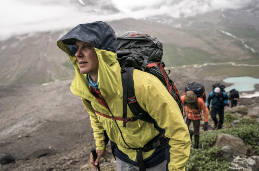 Four hikers with large backpacks trek up a hill in the rain in Greenland.