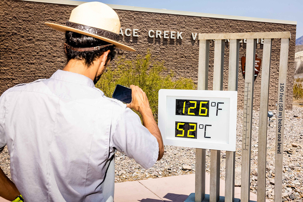 A park ranger taking a photograph of a digital thermometer that shows temperatures are 126 degrees Farenheit.