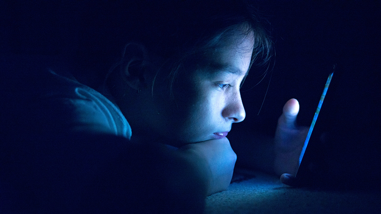 Photo of a young person in the dark, staring at a mobile device.