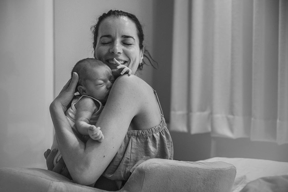 Mother holding baby to her heart and smiling with closed eyes