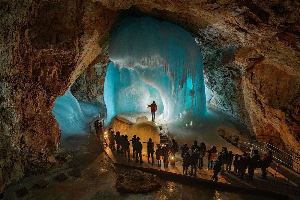 A crowd stands around a large pillar of ice in a cave