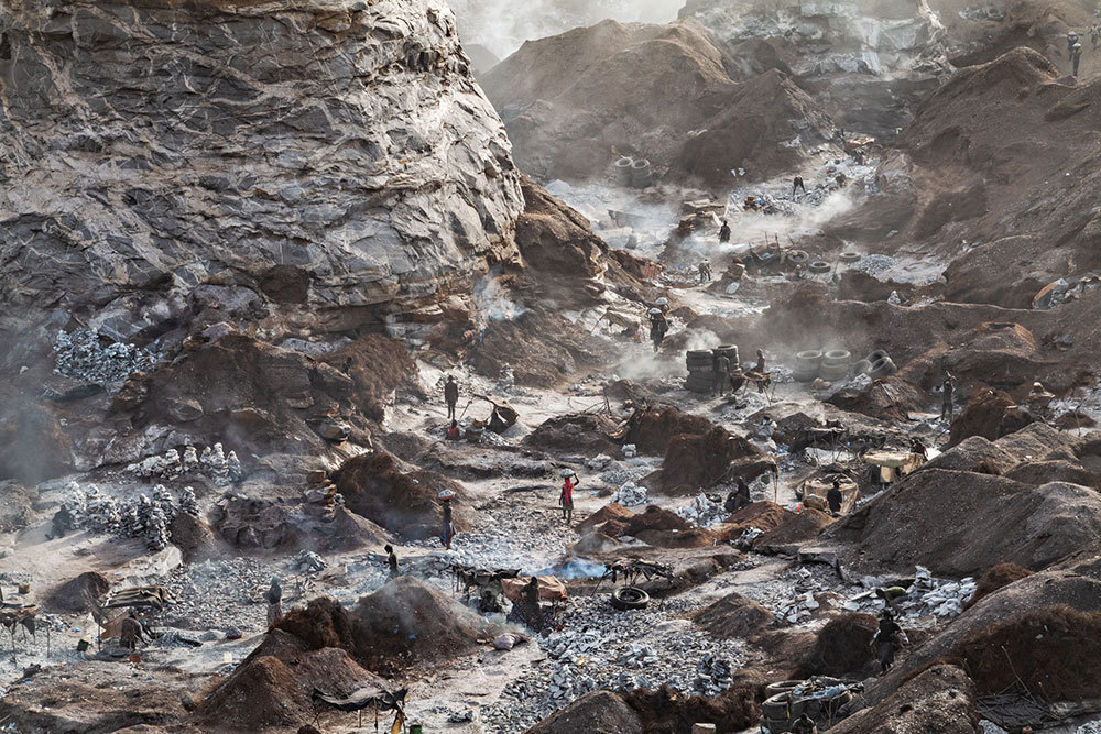 A picture of a quarry with men and women working and smoke along the bottom