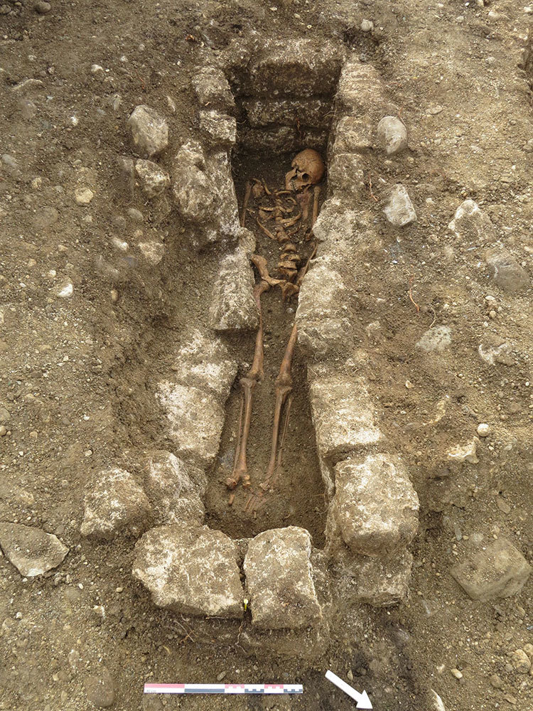 A picture of a skeleton in a hole surrounded by large stones